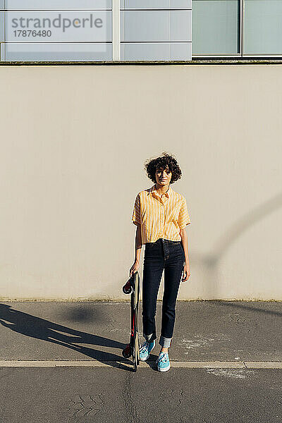 Woman with skateboard standing in front of wall