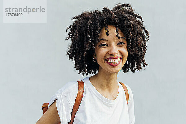 Happy woman with curly hair in front of wall
