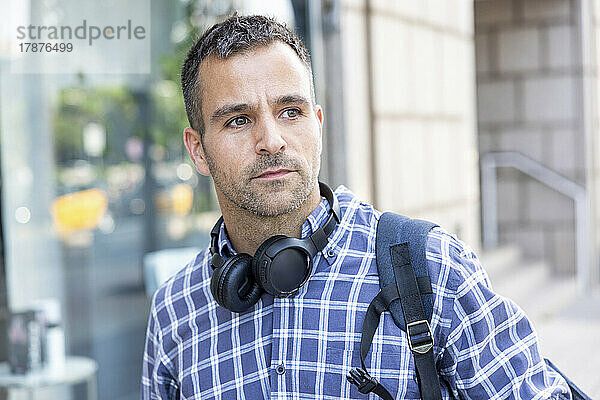 Reifer Mann mit kabellosen Kopfhörern und kariertem Hemd