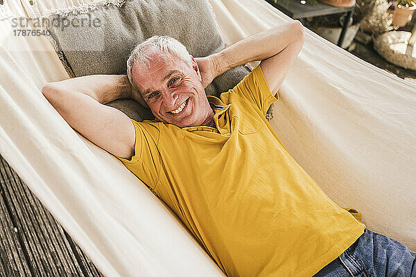 Smiling man with hands behind head resting in hammock