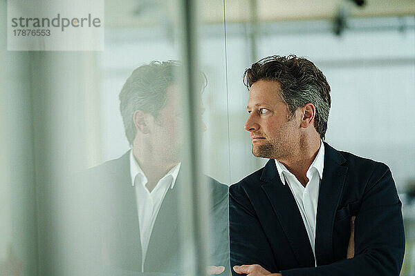 Thoughtful mature businessman looking through glass wall