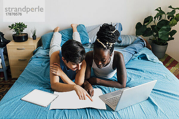 Lesbisches Paar mit Kartenplanungsreise auf dem Bett liegend