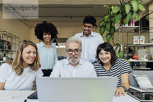 Lächelnde Kollegen mit Manager  der Laptop bei Besprechung im Büro nutzt