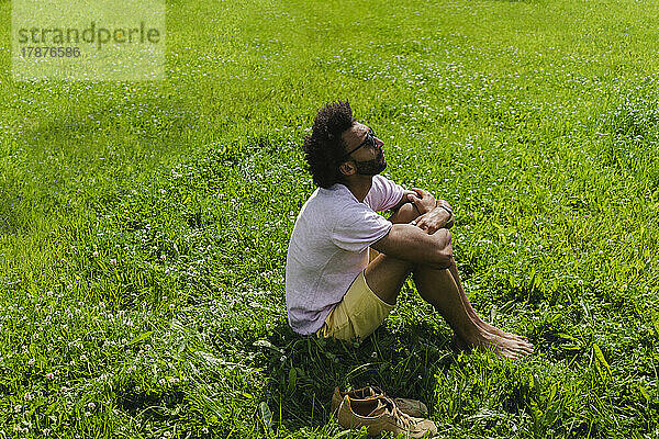 Mann umarmt Knie  sitzt auf Gras im Park