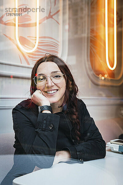 Glückliche Frau mit Brille sitzt am Tisch im Café