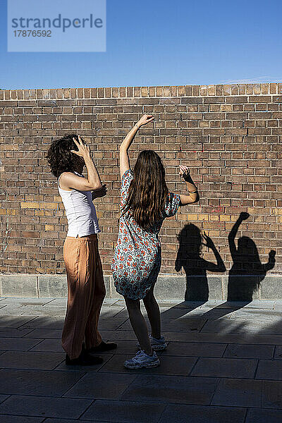 Young couple dancing in front of wall on sunny day
