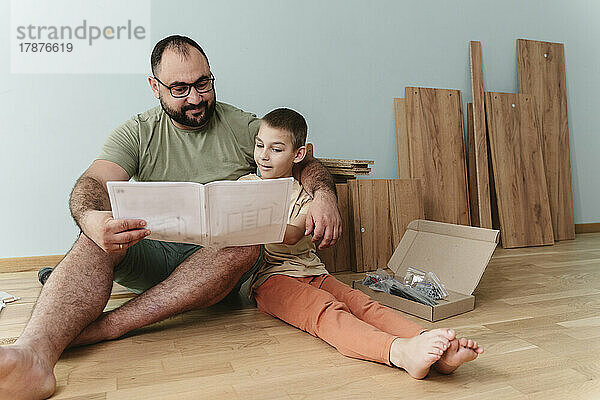 Glücklicher Vater mit Sohn  der zu Hause auf dem Boden sitzt und die Bedienungsanleitung liest