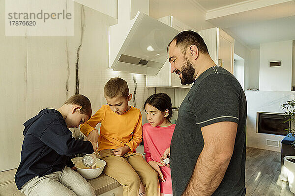 Happy father assisting children in preparing omelet at home