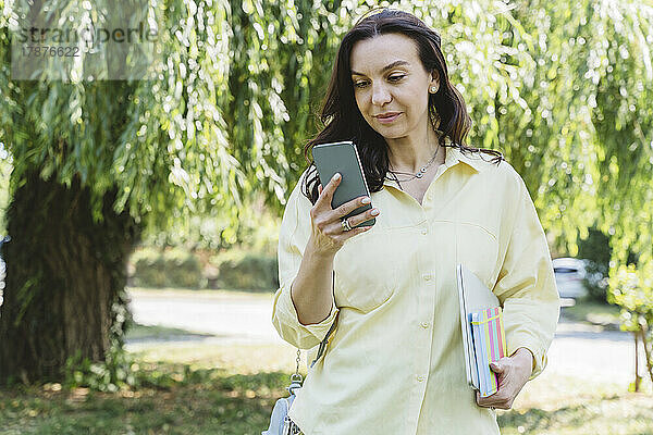Frau mit Laptop und Tagebuch nutzt Smartphone im Park
