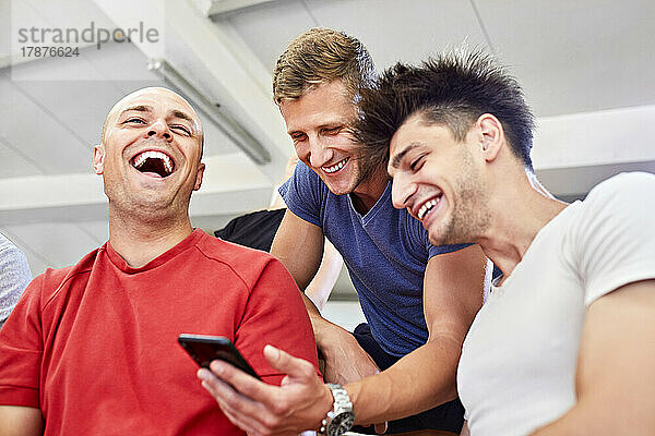 Fröhliche Freunde  die im Stadion ihr Smartphone teilen