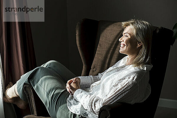 Happy mature woman relaxing in armchair at home