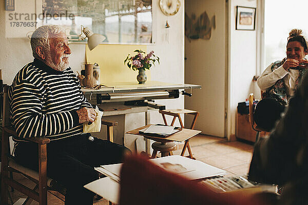 Lächelnder älterer Mann  der zu Hause bei Künstlern sitzt