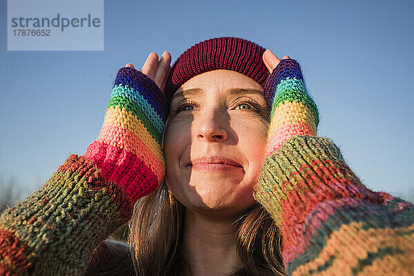 Lächelnde Frau mit Regenbogenhandschuhen  die ihr Gesicht berührt