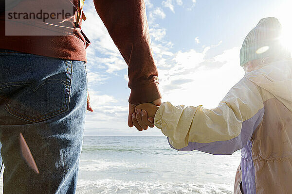 Vater hält an einem sonnigen Tag die Hand seiner Tochter am Strand