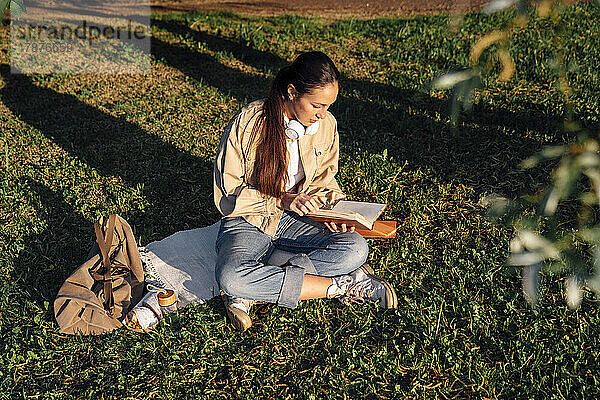 Frau sitzt auf Gras und liest Buch im Park