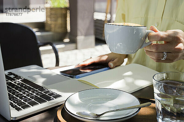 Hand eines Freiberuflers mit Kaffeetasse im Straßencafé