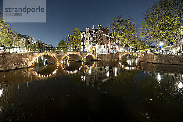 Niederlande  Nordholland  Amsterdam  beleuchtete Bogenbrücke  die sich nachts über den Stadtkanal erstreckt
