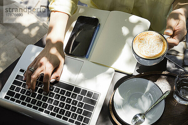 Freiberufler mit Kaffeetasse und Laptop im Straßencafé