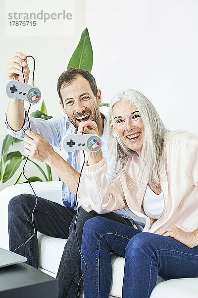 Glückliche Mutter und Sohn zeigen Gamecontroller  die zu Hause auf dem Sofa sitzen