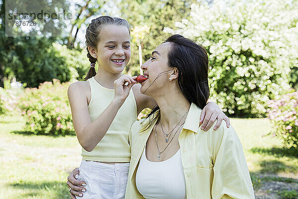 Glückliche Tochter füttert Mutter am Wochenende im Park mit Erdbeeren