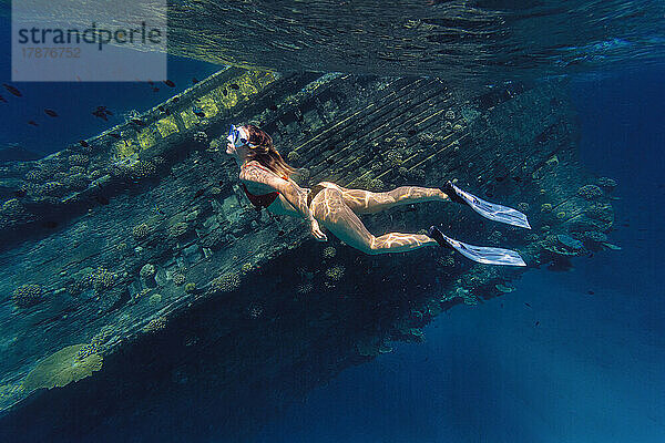 Frau schwimmt vor Schiffswrack im Meer