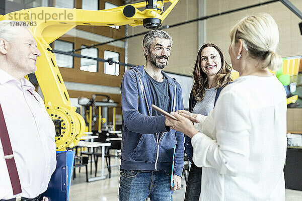 Techniker schütteln einem älteren Kollegen bei einem Treffen in der Fabrik mit Industrierobotern die Hand