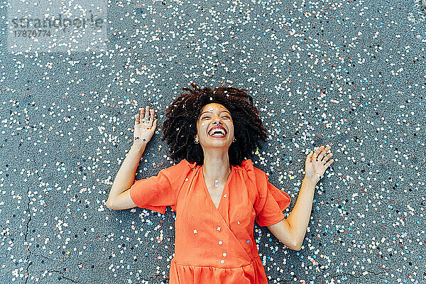 Cheerful young woman with confetti lying on road