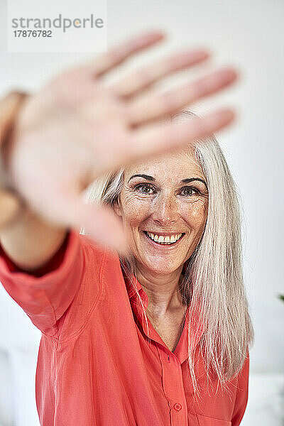Happy mature woman showing stop gesture in front of wall