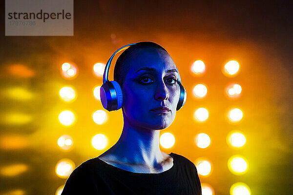 Ernsthafte junge Frau mit Kopfhörern vor Neonlichtern