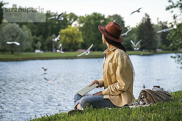 Frau mit Laptop sitzt am See im Park