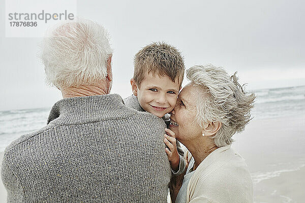 Glückliche Großeltern verbringen schöne Zeit mit ihrem Enkel am Strand