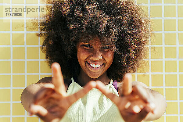Lächelndes Mädchen mit Afro-Frisur  das ein Friedenszeichen zeigt