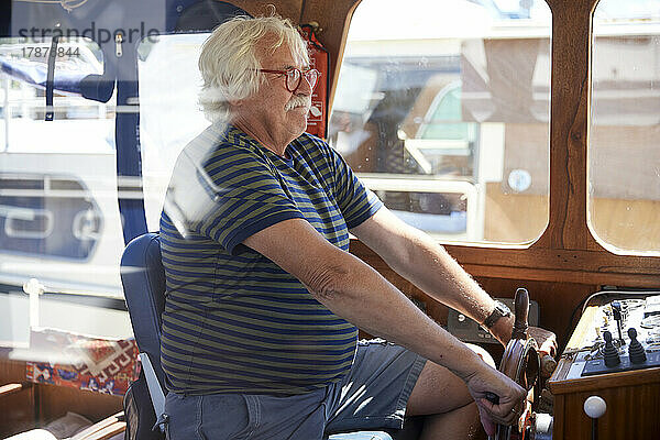 Älterer Mann hält im Urlaub das Ruder eines Segelmotorboots
