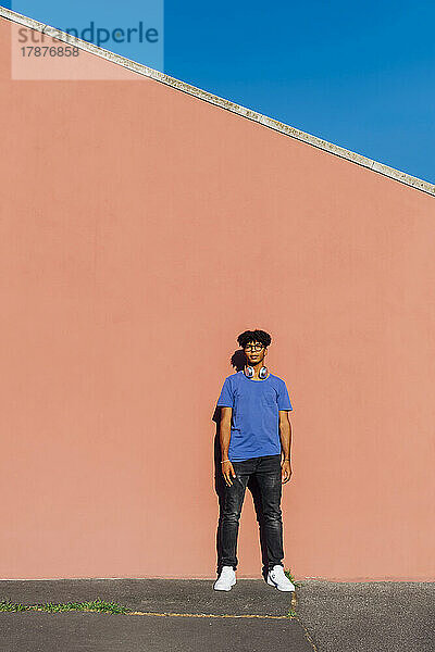 Young man standing in front of wall on sunny day