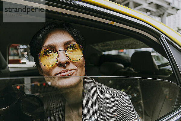 Nachdenkliche Geschäftsfrau mit gelber Sonnenbrille sitzt im Auto