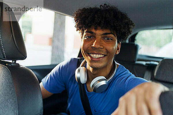 Glücklicher Mann mit kabellosen Kopfhörern sitzt im Auto