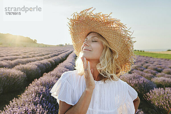 Lächelnde Frau mit geschlossenen Augen  die ihr Kinn im Lavendelfeld berührt