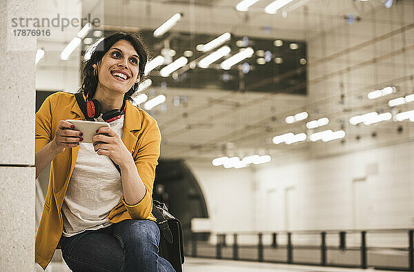 Lächelnde Transgender-Geschäftsfrau mit Telefon und Blick auf die U-Bahn-Station