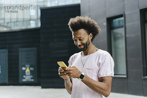 Lächelnder Mann benutzt Mobiltelefon in der Nähe eines Gebäudes