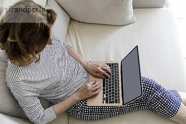 Reife Frau sitzt zu Hause im Wohnzimmer und benutzt Laptop