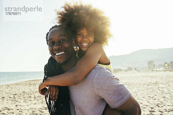 Glücklicher Vater huckepack  Afro-Tochter am Strand