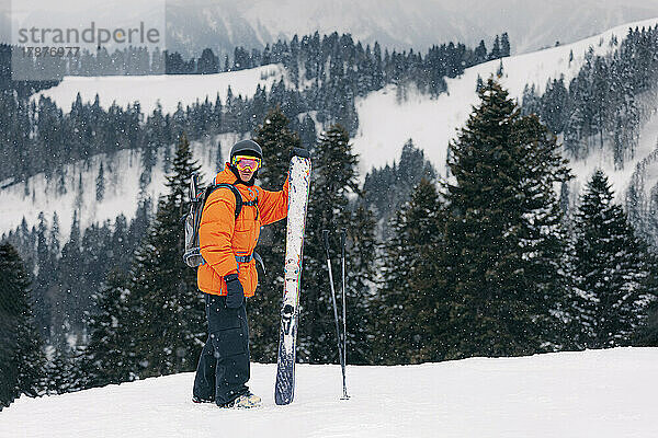 Skifahrer mit Ski und Stöcken steht vor Bergen