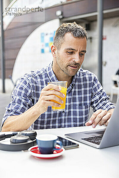 Reifer Freiberufler trinkt Orangensaft mit Laptop im Café