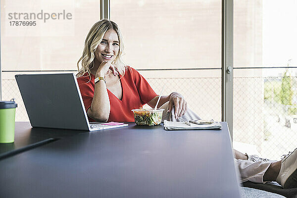 Geschäftsfrau sitzt mit Laptop und Lunchbox am Schreibtisch im Büro