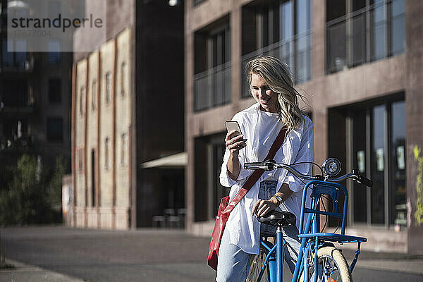 Glückliche junge Frau  die ihr Mobiltelefon auf dem Fahrrad benutzt