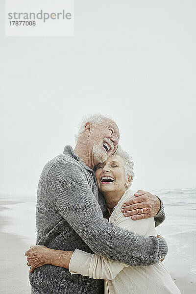 Laughing senior couple embracing at the sea