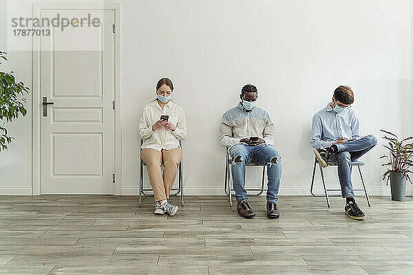 Menschen mit Gesichtsmasken sitzen auf Stühlen im Wartebereich