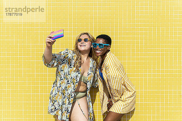 Glückliche Frau macht Selfie mit Freund vor gelber Wand