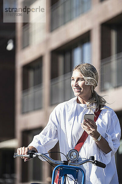 Glückliche Frau mit Fahrrad und Smartphone an einem sonnigen Tag