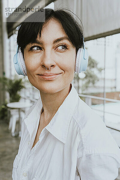 Lächelnde Geschäftsfrau mit kurzen Haaren  die über kabellose Kopfhörer Musik hört